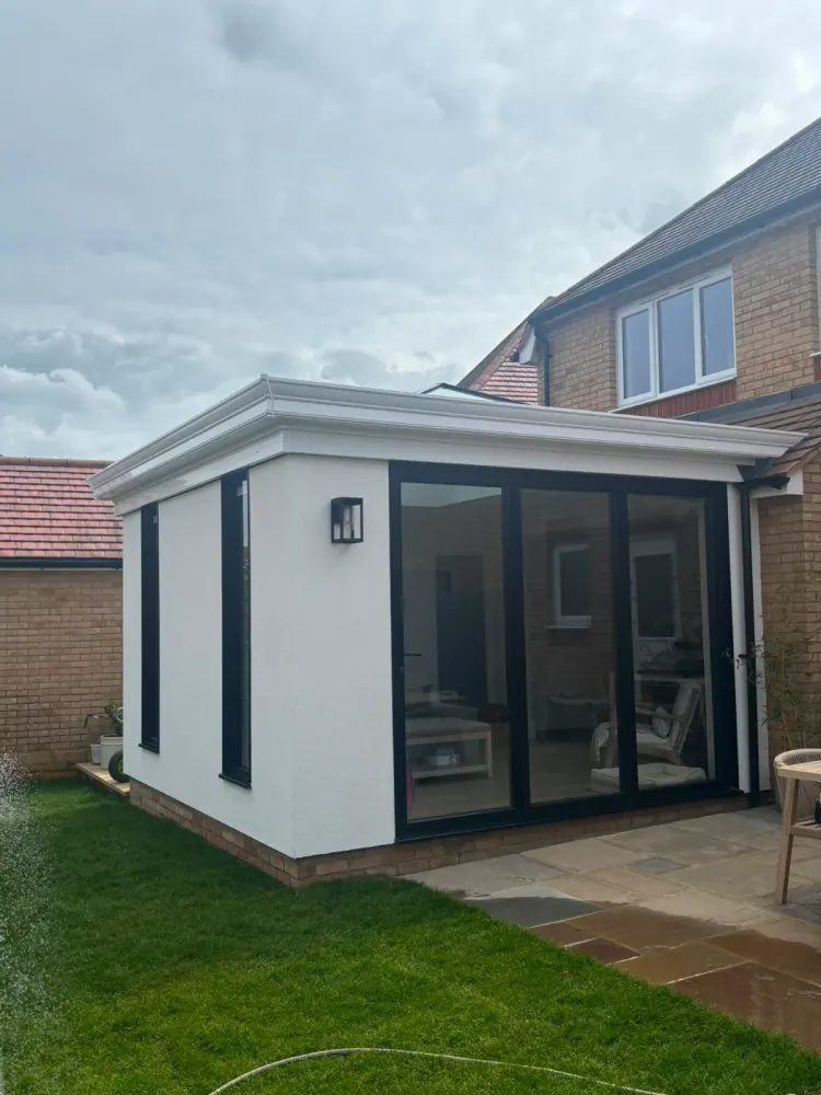 White-rendered flat-roof extension with a slim parapet and anthracite sliding doors