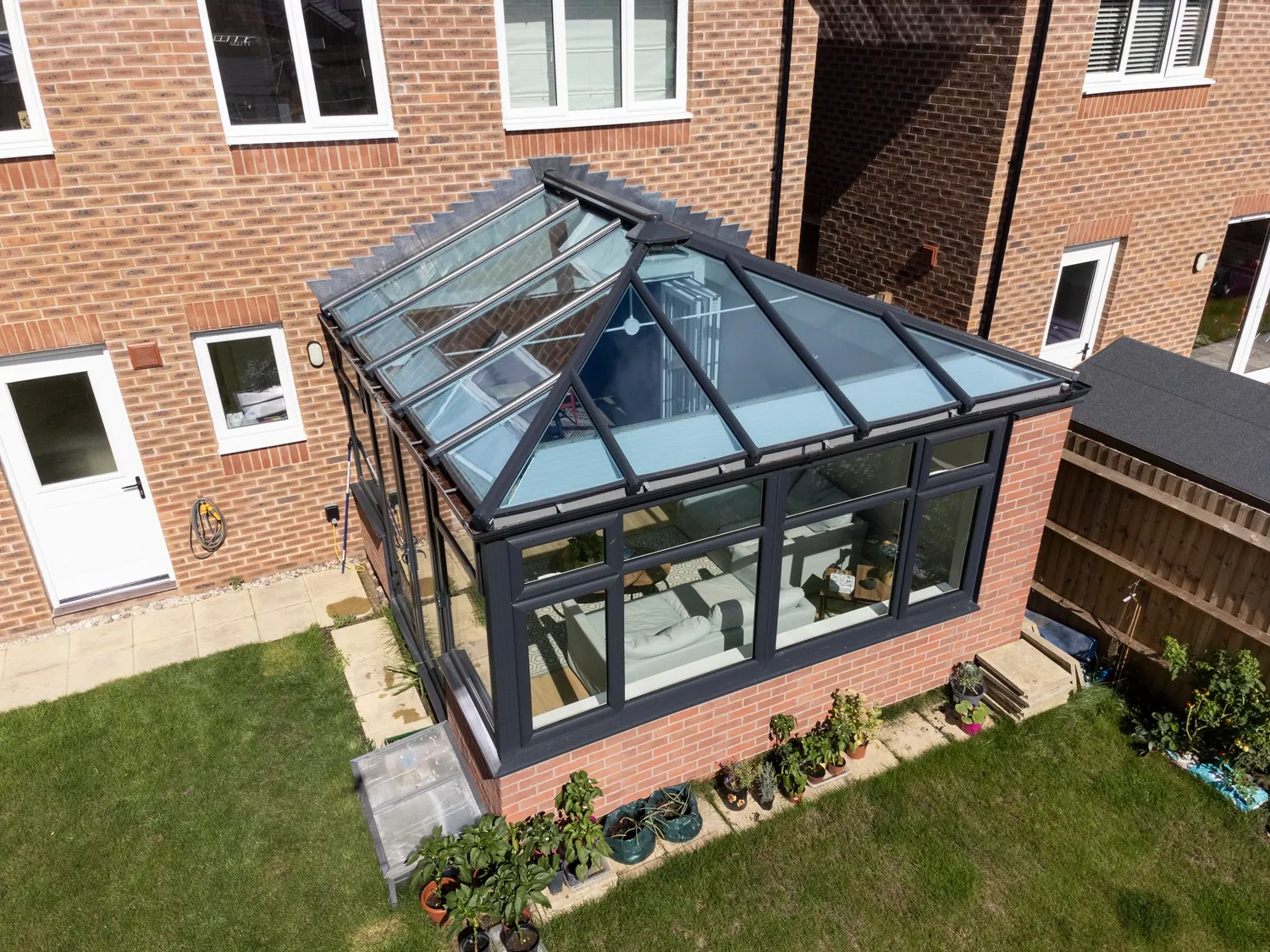 Aerial view of a completed modular extension with an anthracite glazed lantern roof set against a brick home and garden