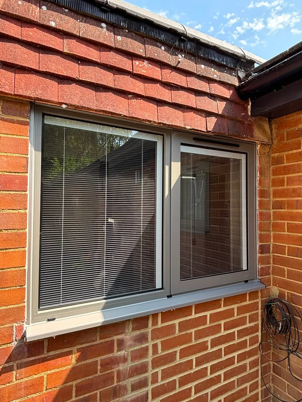 Grey-framed casement window with integral blinds, fitted to a red-brick home