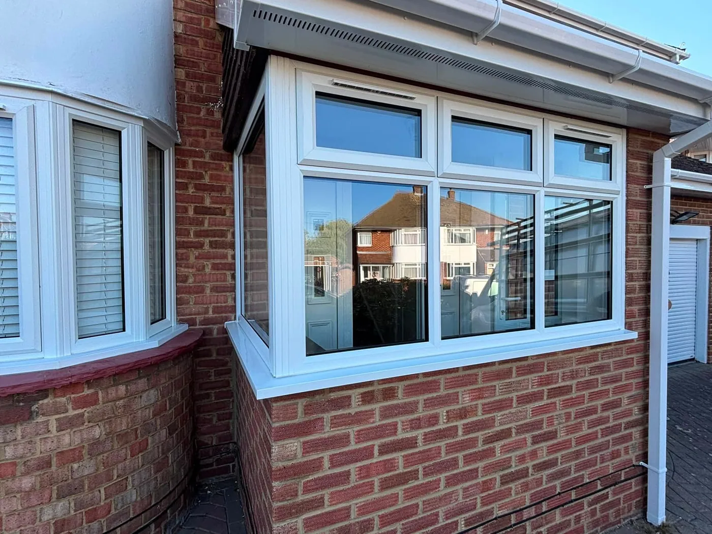 White UPVC casement window with top opening lights, fitted alongside a bay window on a red-brick bungalow