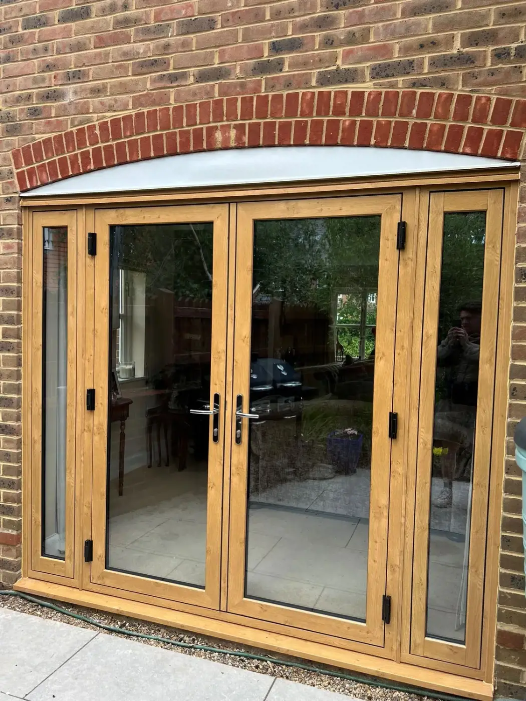 Oak-effect bifold doors set under a brick arch, viewed from the garden