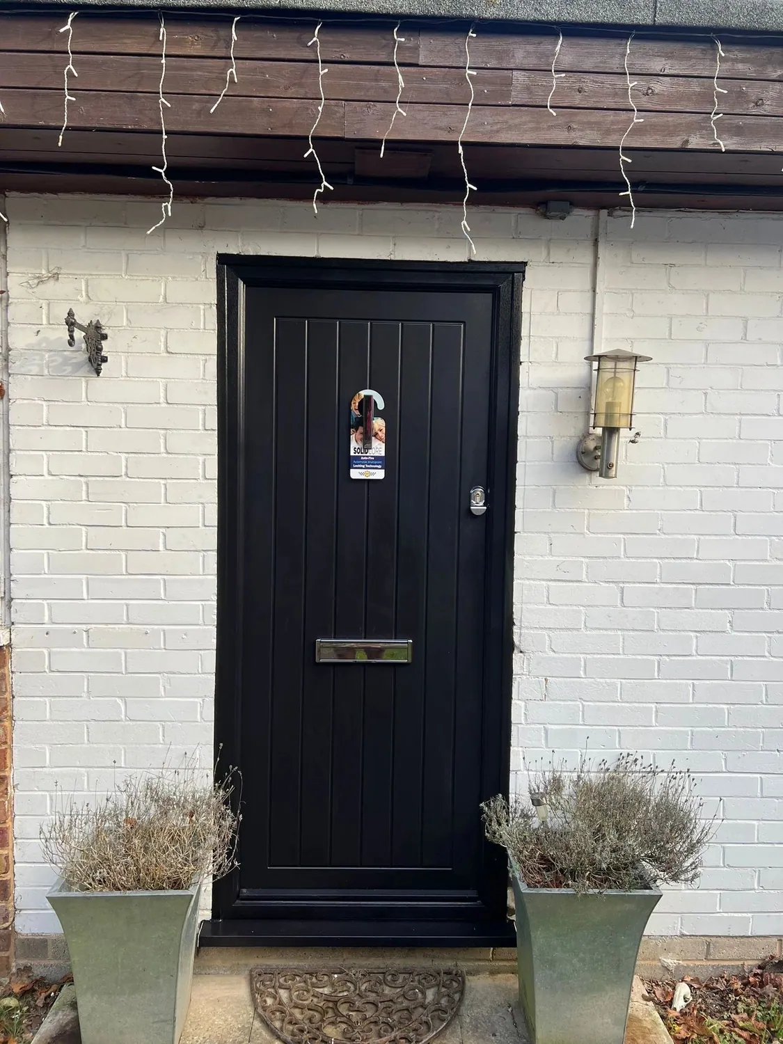 Black composite front door with a flush vertical-board finish on a white brick house