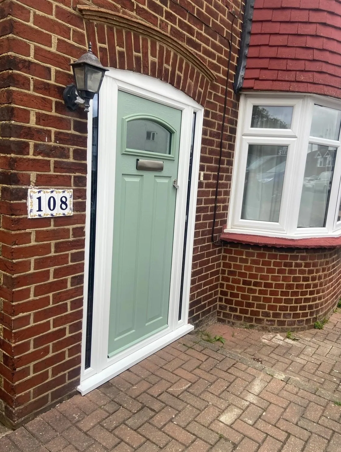 Sage green composite front door with arched glazing, beside a white bay window