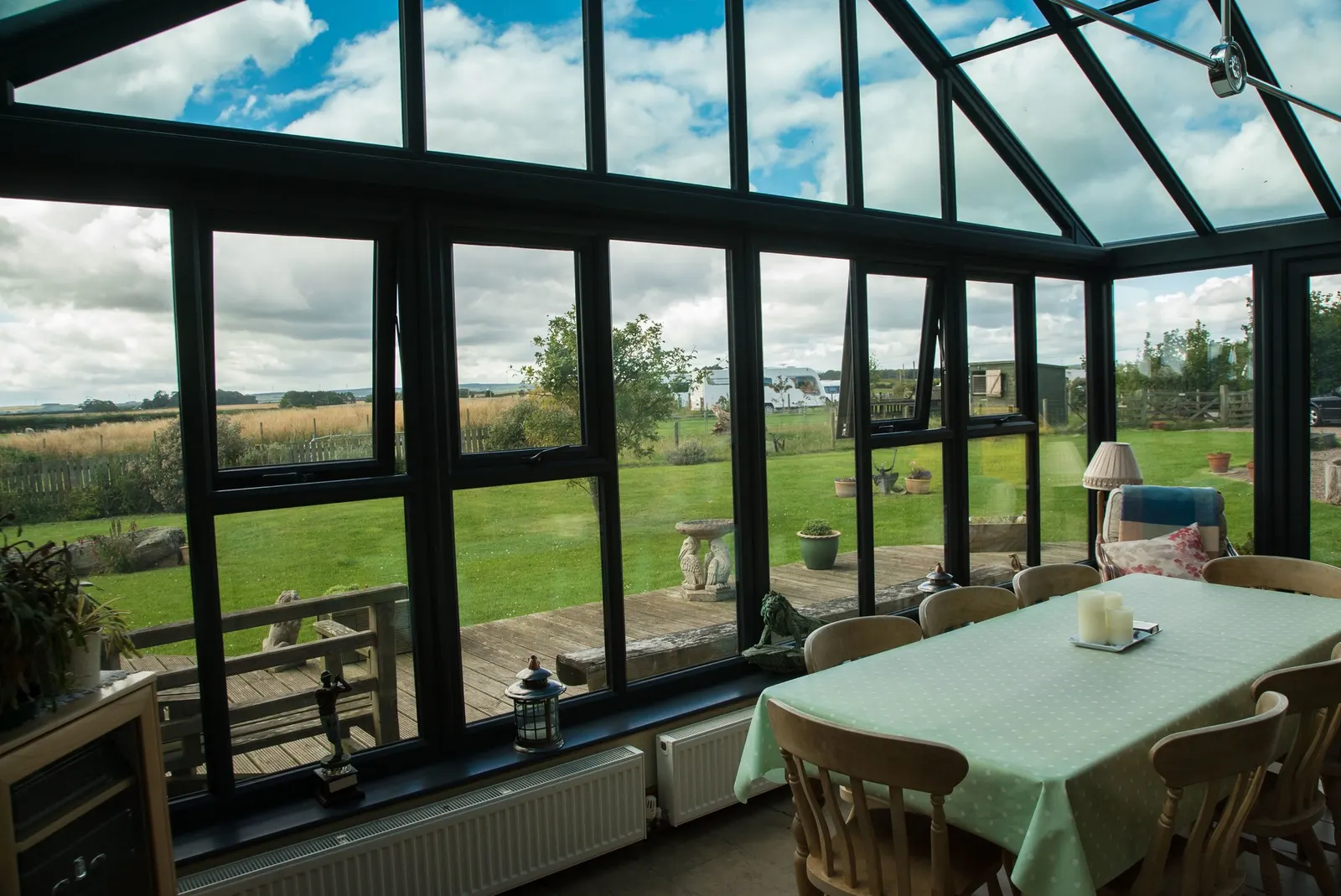 An anthracite-framed conservatory from the inside, glazed roof above a dining table, fields beyond