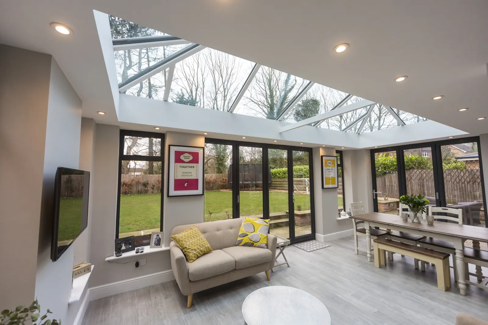 An open-plan room under a white roof lantern, with anthracite bifold doors onto the garden