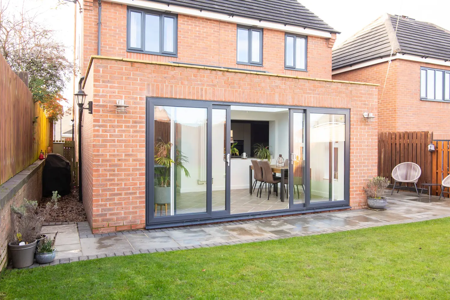 Anthracite aluminium sliding patio doors across the back of a red brick extension, seen from the lawn