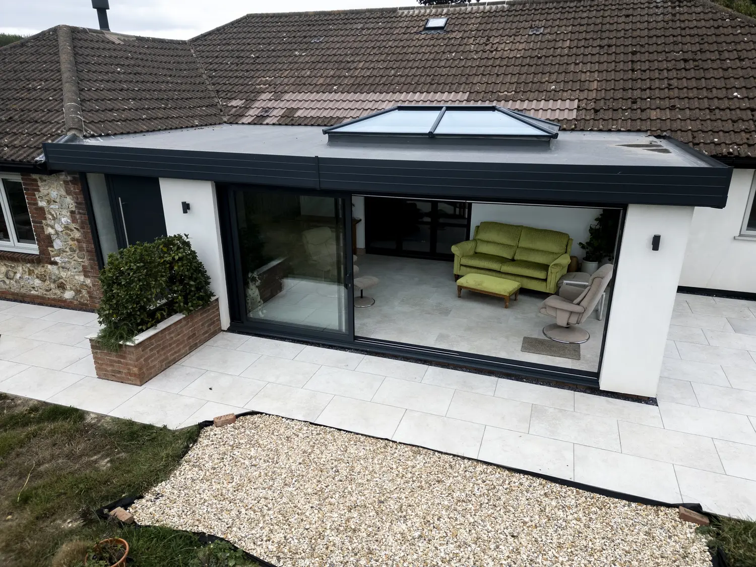 Anthracite sliding patio doors slid open across the back of a single-storey extension with a flat warm roof and a roof lantern, onto a paved patio