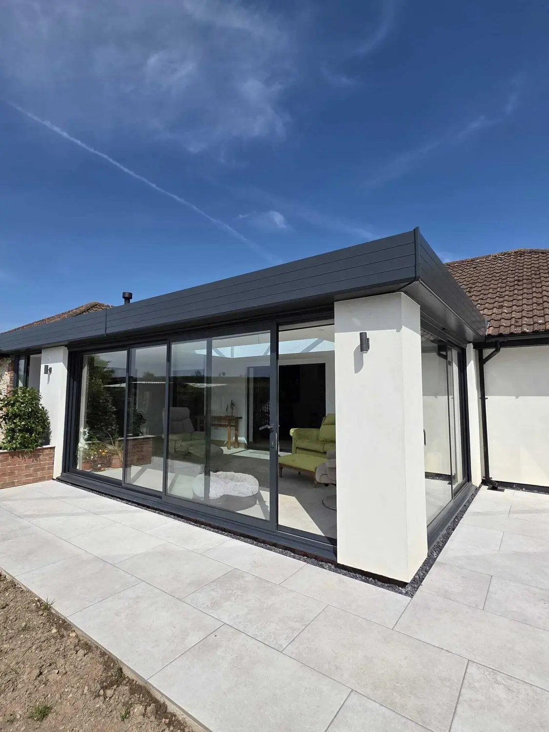 A three-panel anthracite sliding patio door run along a flat-roof extension, with glazing returning around the corner