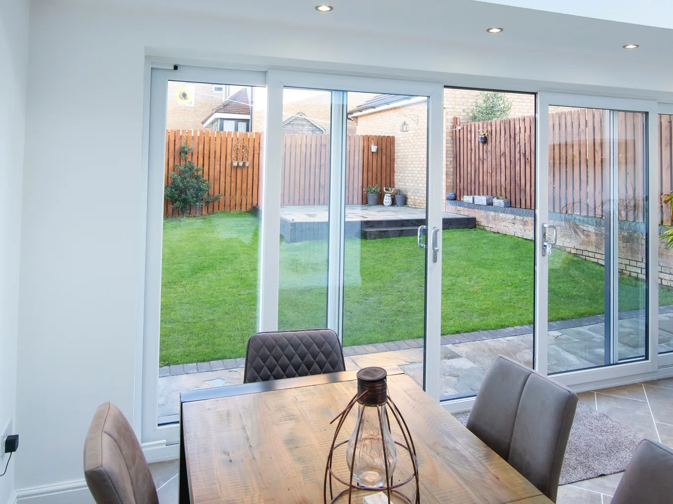 White UPVC sliding patio doors across the back of a dining room, open onto a lawn