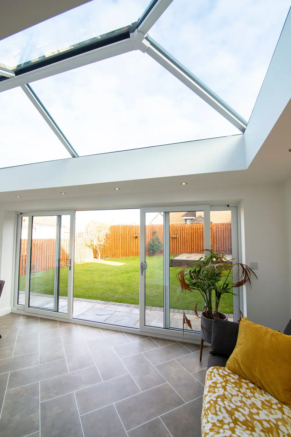 A four-panel white sliding patio door run seen from inside, with a roof lantern above and a garden beyond
