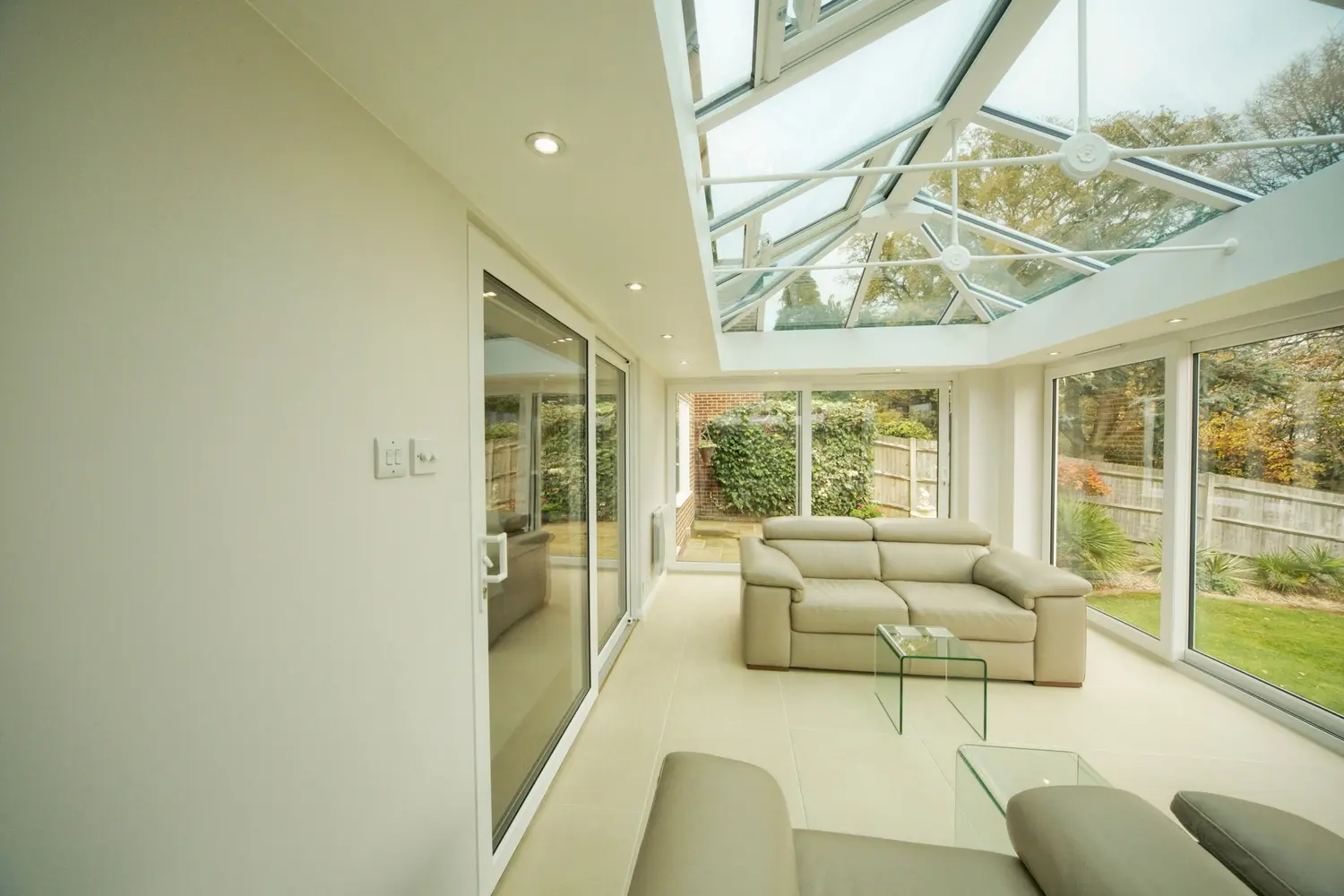 A white-framed glazed room with sliding doors, looking out over an open aspect of lawn and fields