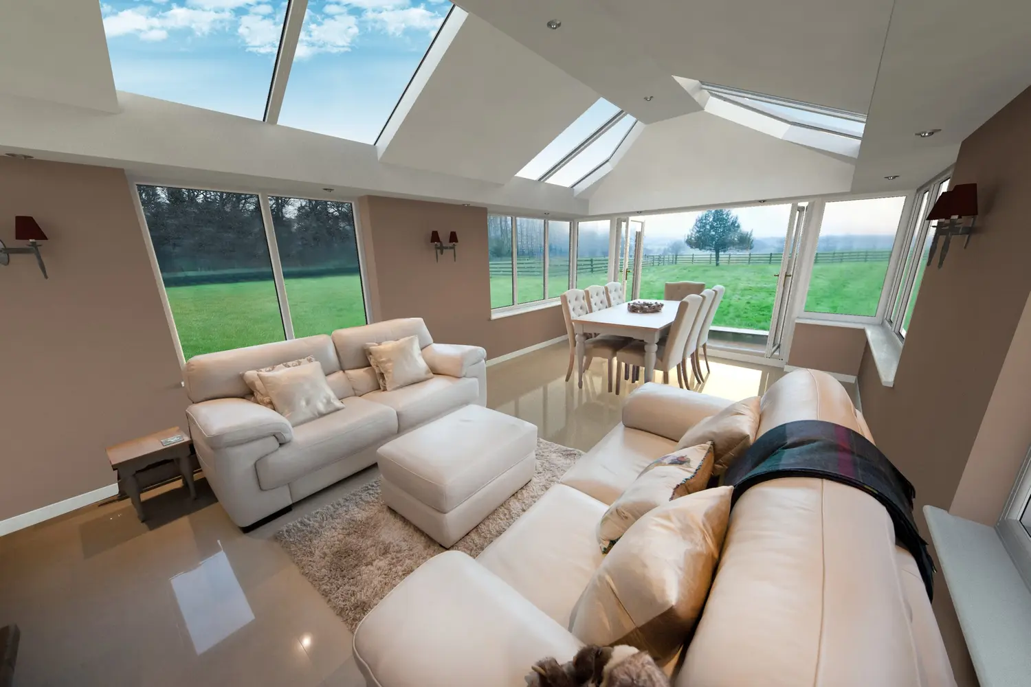 A lounge under a glazed roof with windows on two sides, looking out over fields