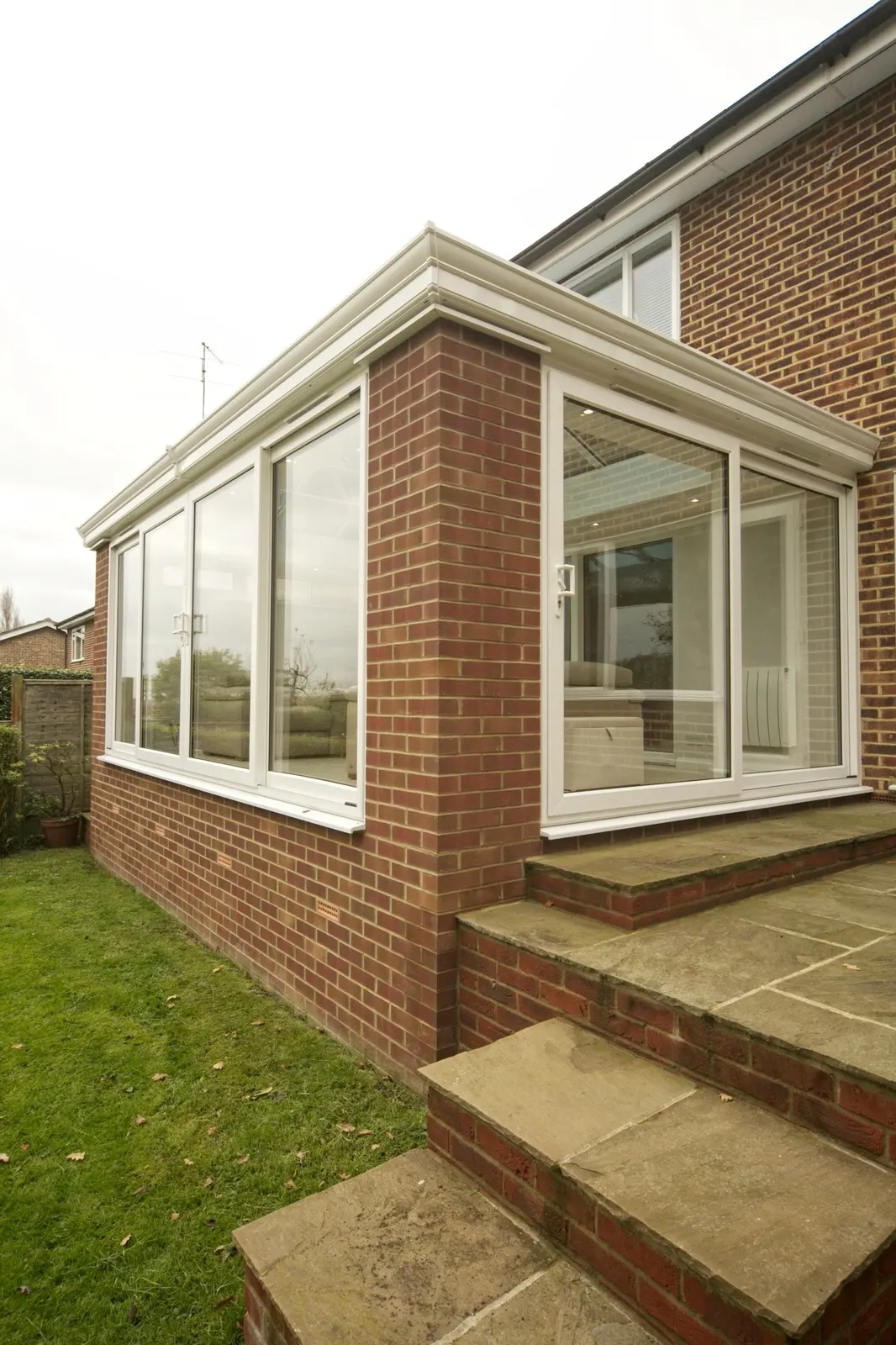 A run of large white UPVC windows across the side of a brick sunroom, with stone steps to the garden