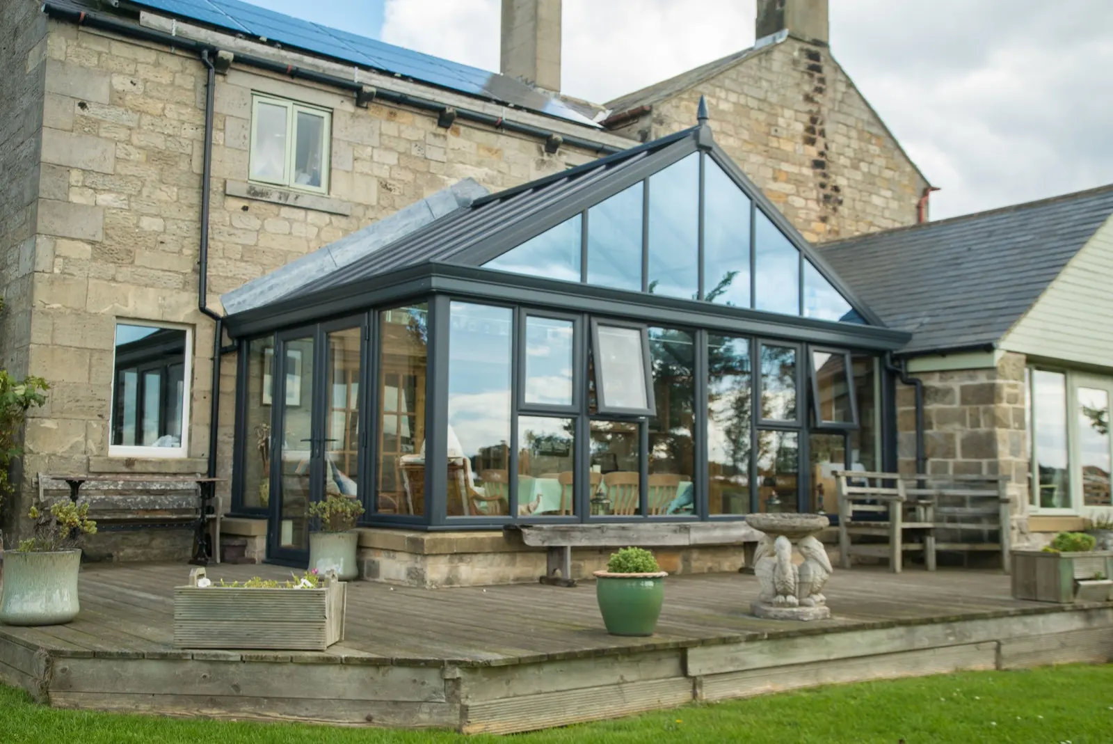 An anthracite gable-end conservatory with a solid roof, on a stone house