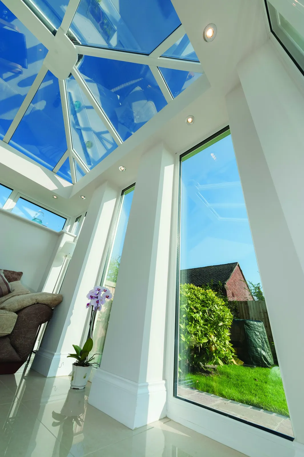 A tall glazed gable and roof lantern seen from inside, with full-height windows onto a garden