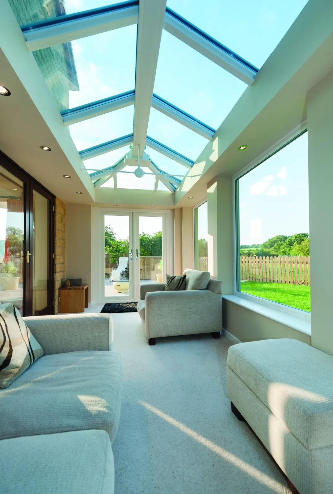 A lounge under a white glazed lantern roof, opening onto a garden through patio doors