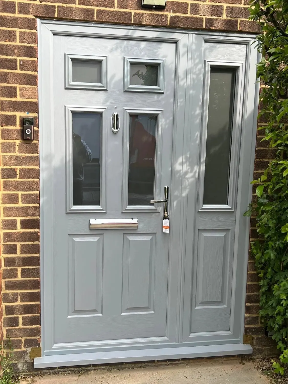 A grey composite front door with glazed panels and a matching glazed side panel