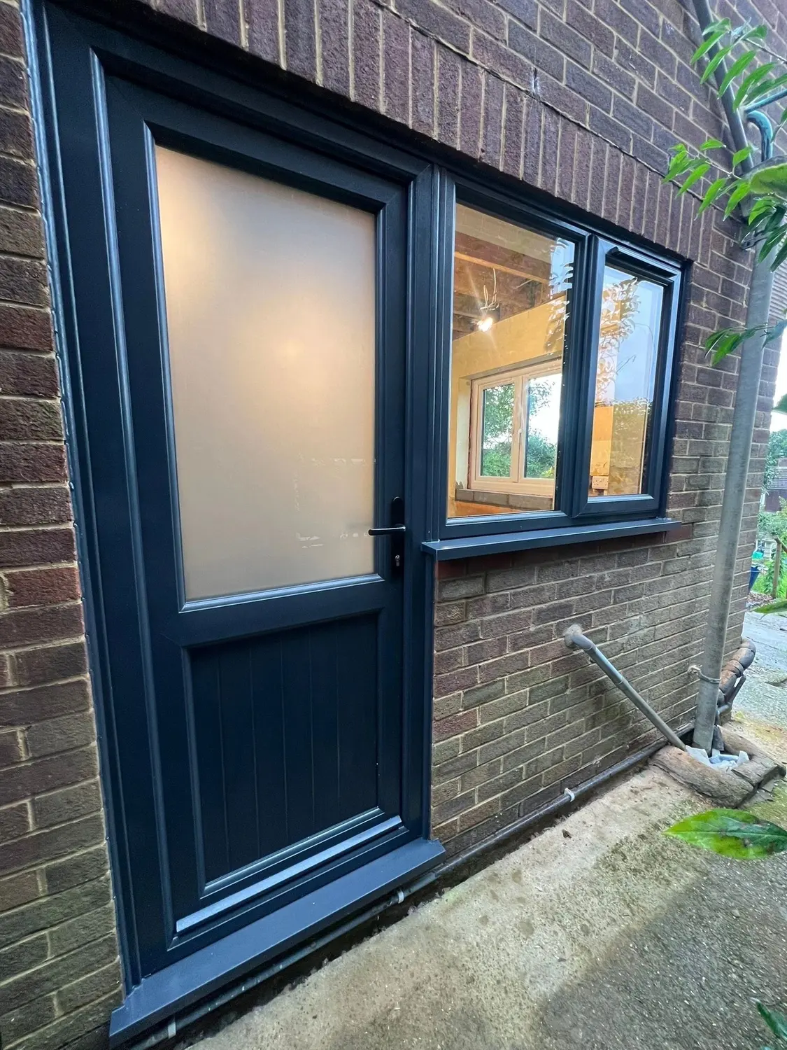 A navy composite door with obscure glazed panels and a side window, in red brickwork