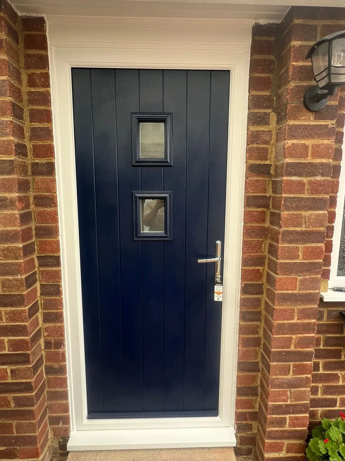 A navy composite front door with two square glazed panes, in a brick opening