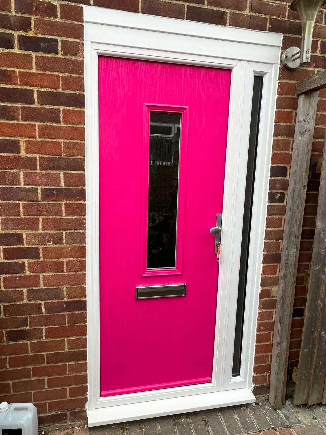 A bright pink composite front door with a glazed side panel, in red brickwork