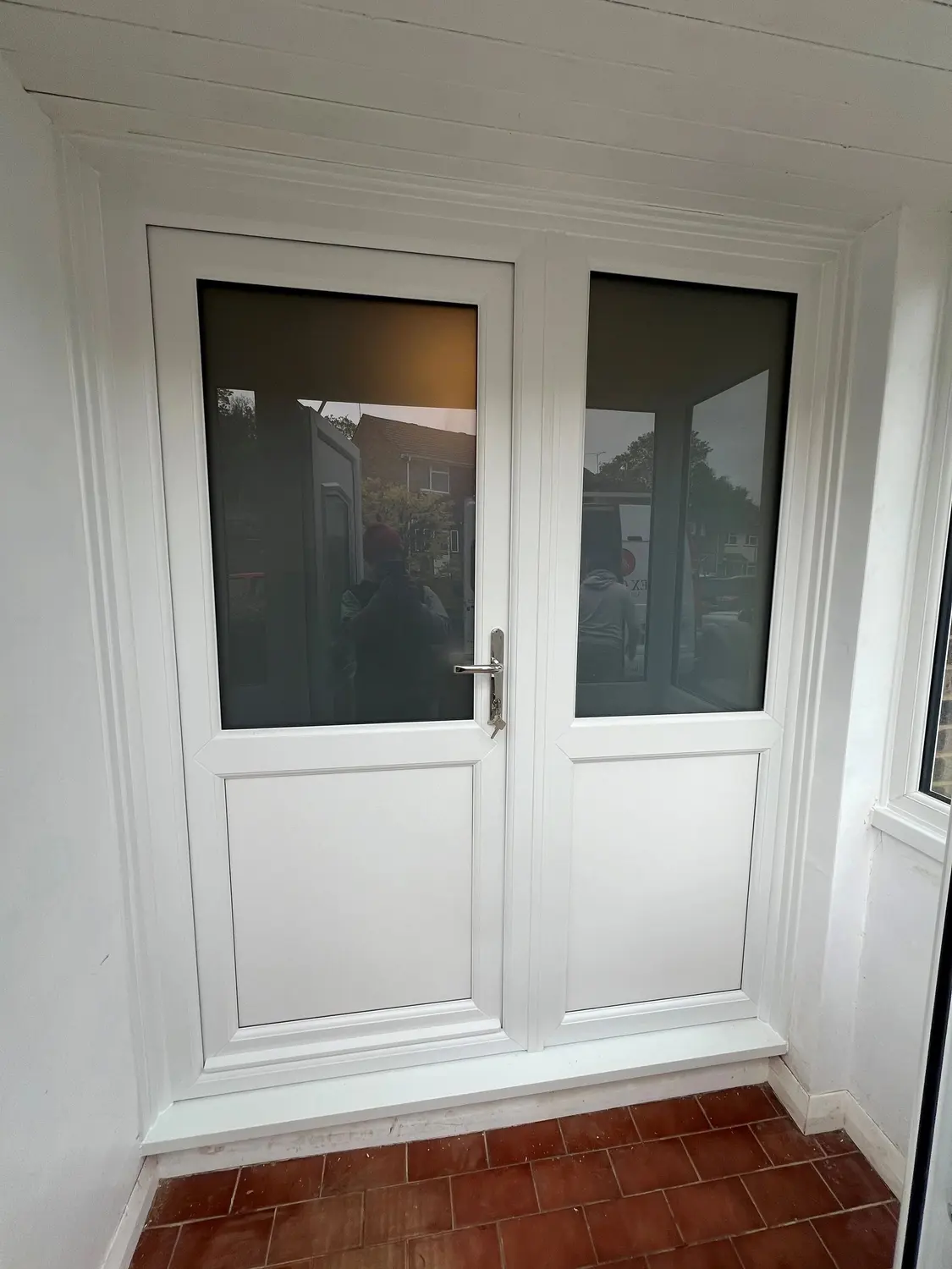 A white UPVC double door with glazed panels, in a tiled porch