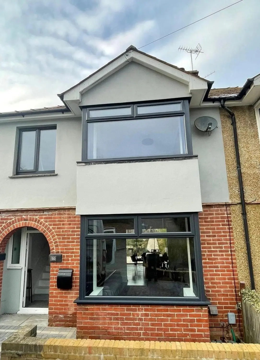 An anthracite bay window and a sage green front door on a part-rendered house