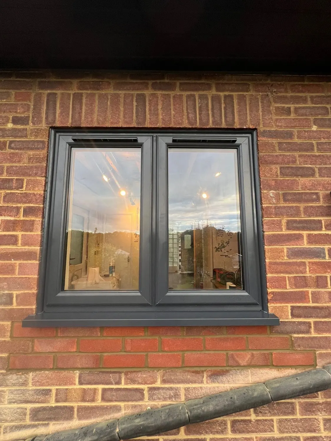An anthracite UPVC casement window with two opening lights, in red brickwork
