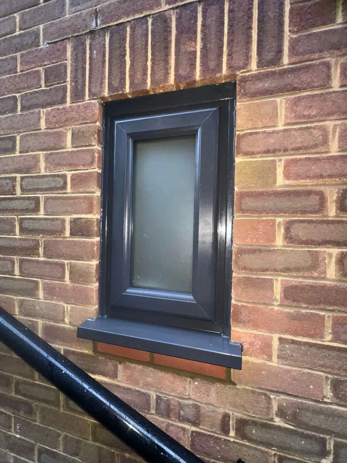 An anthracite UPVC window with obscure glazing, in red brickwork
