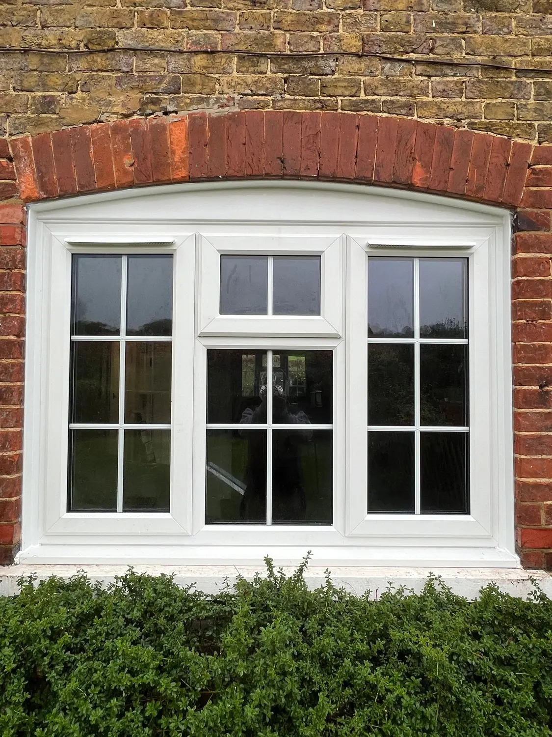 A white UPVC bay window with Georgian bars, set under a brick arch