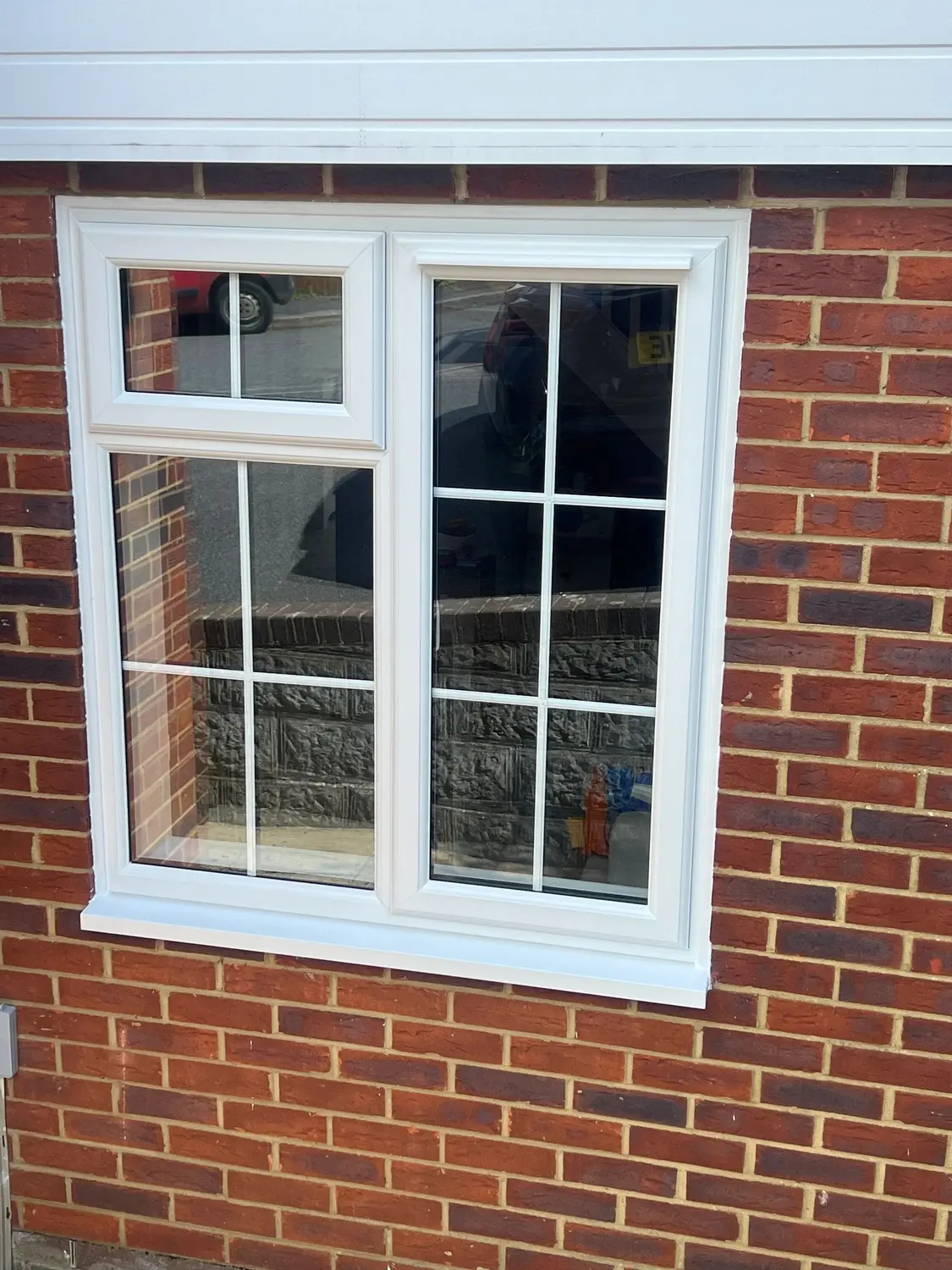 A white UPVC casement window with Georgian bars, fitted in red brickwork