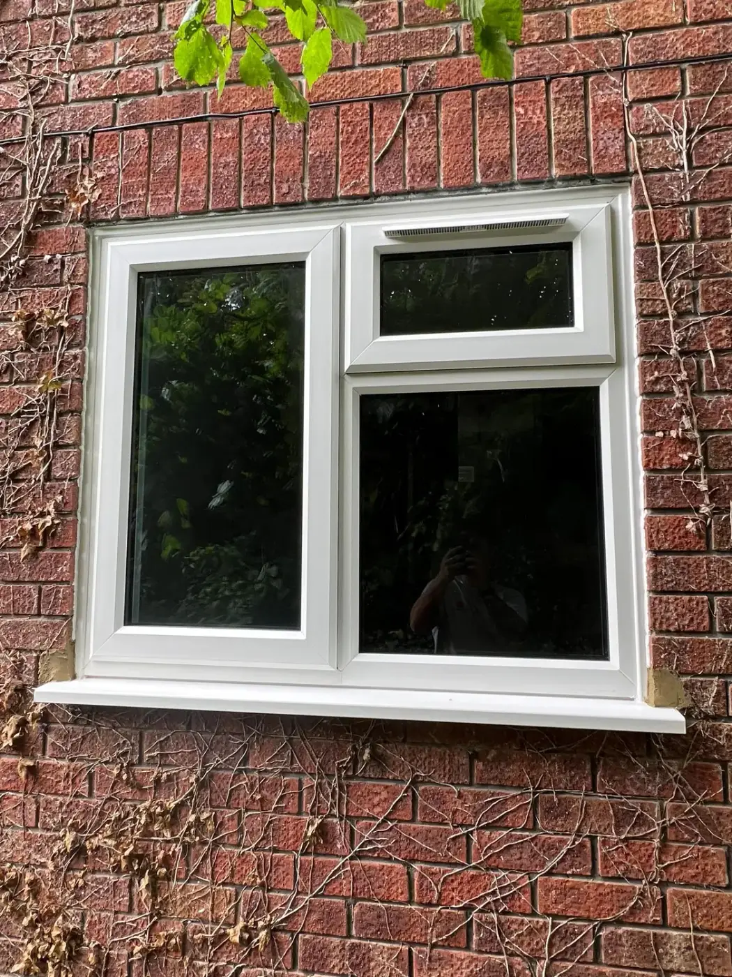 A white UPVC casement window with a top light, in red brickwork