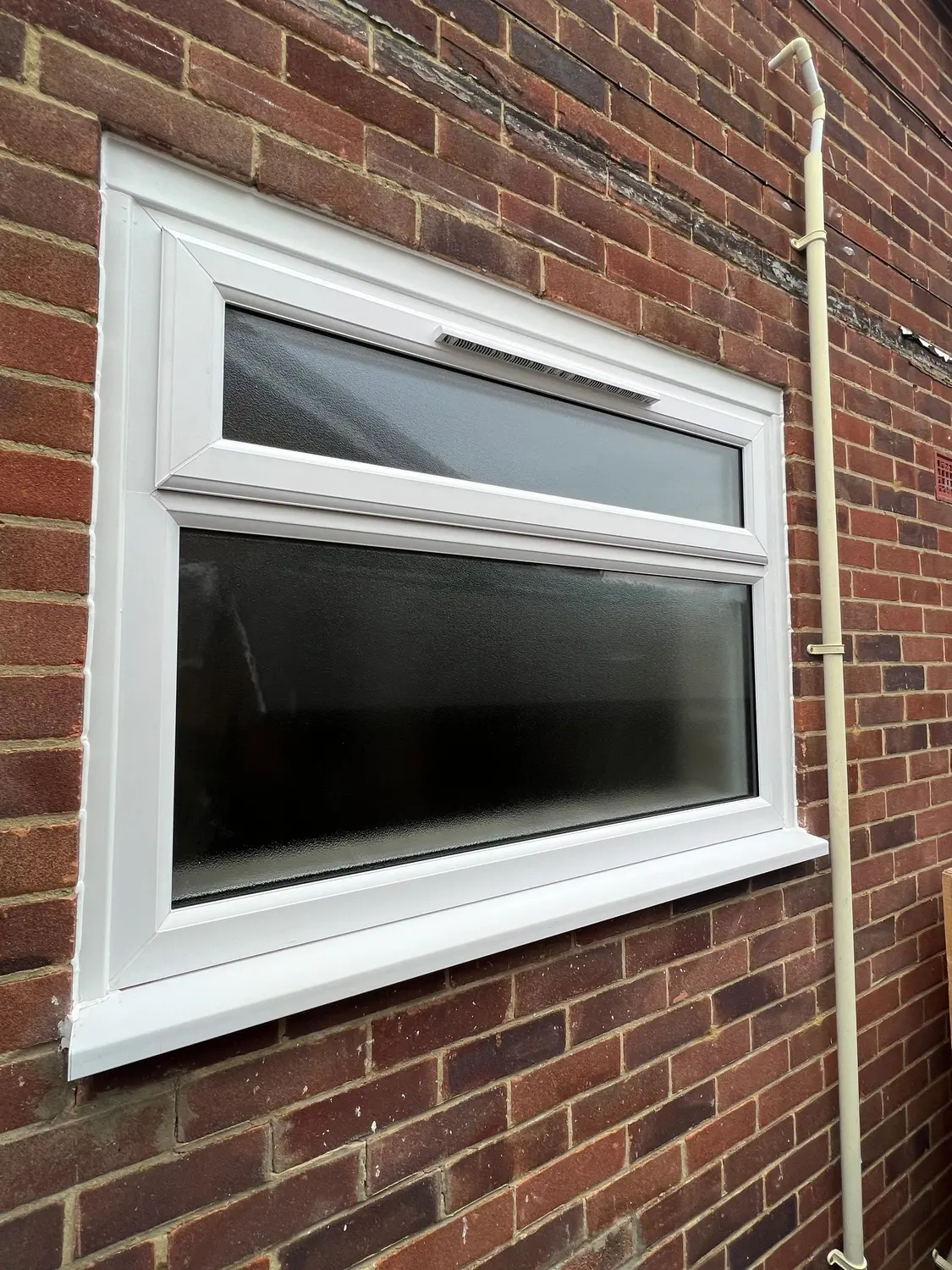 A white UPVC window with a top opening light, in red brickwork