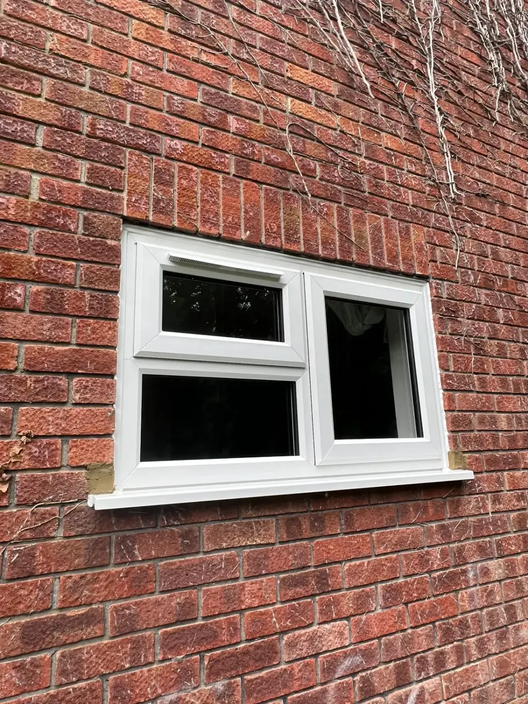 A white UPVC window with two top opening lights, in red brickwork