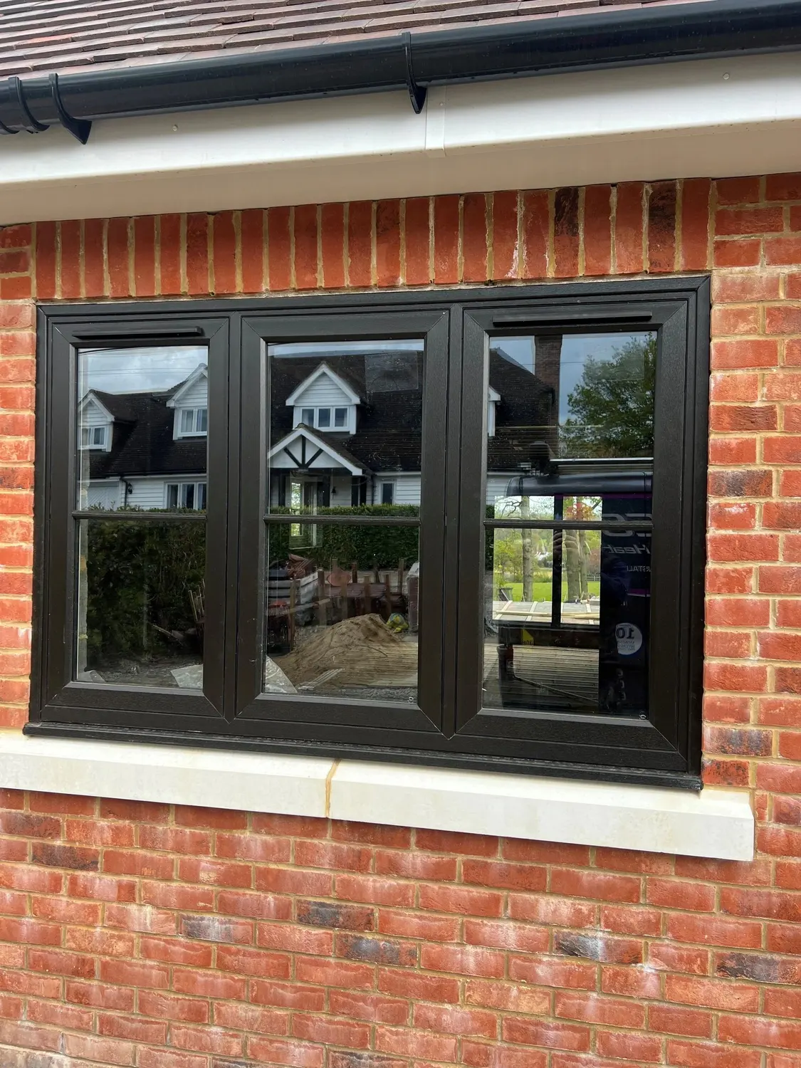 A dark woodgrain UPVC casement window in red brickwork